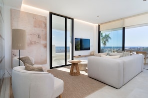 A modern living room with a sofa, armchair, and a TV on a wall. - Penthouse with Panoramic Sea Views in Estepona (Estepona)
