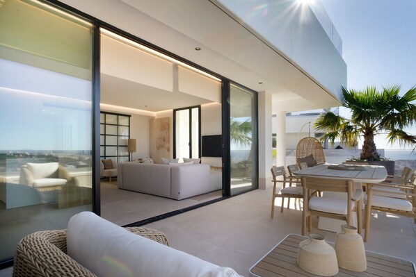 A modern living space with a glass wall, a sofa, a dining table, and a view of the ocean. - Penthouse with Panoramic Sea Views in Estepona (Estepona)