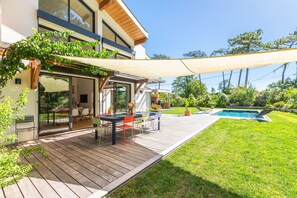 Una casa moderna con terraza, mobiliario exterior, piscina y jardín.