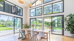 Un intérieur moderne avec une table à manger en bois, des chaises grises, de grandes fenêtres et une plante en pot.