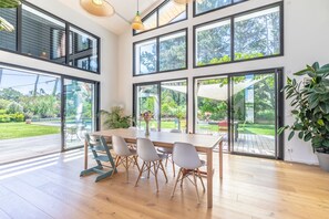A modern interior with a wooden dining table, grey chairs, large windows, and a potted plant. - Fairway Villa - À 5 min des plages et du golf (Anglet)