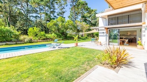 Une maison moderne dotée d’une piscine, de meubles de jardin et d’une pelouse bien entretenue.