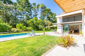 Une maison moderne dotée d’une piscine, de meubles de jardin et d’une pelouse bien entretenue.