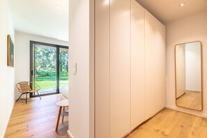 Una habitación moderna con un amplio ventanal corredera que da a un jardín, suelo de madera, sofá blanco, una mesita pequeña y un espejo grande.