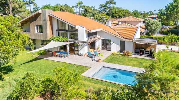 Una casa moderna con piscina, un patio con mobiliario exterior y un jardín amplio.