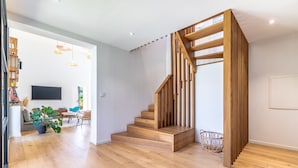 Un intérieur moderne avec un escalier en bois, un téléviseur à écran plat, un coin repas et une plante en pot.