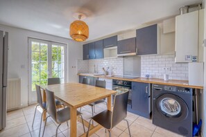 A modern kitchen with a dining table, chairs, a washing machine, and a large window. - Marguerite - Proche de Bordeaux et avec jardin (Pessac)