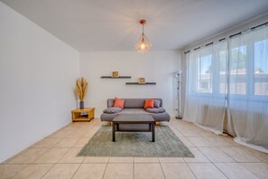 A modern living room with a sofa, coffee table, and decorative items on shelves. - Marguerite - Proche de Bordeaux et avec jardin (Pessac)