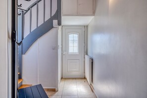 Eine Treppe führt zu einer Tür mit einem Fenster, einem Heizkörper und einer Wandleuchte.
