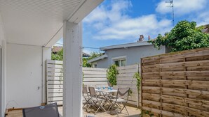 An outdoor patio with a table and chairs, a wooden fence, and a white building in the background. - Le Spatiozo - Appt aux Abatilles, proche plage (Arcachon)