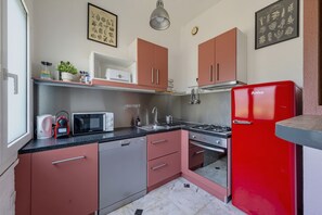 Een kleine keuken met een rode koelkast, roestvrijstalen apparatuur en een magnetron.