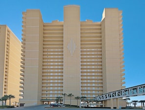 Ein Hochhaus-Hotel mit mehreren Balkonen, einem markanten zentralen Logo und einer Fußgängerbrücke im Vordergrund.
