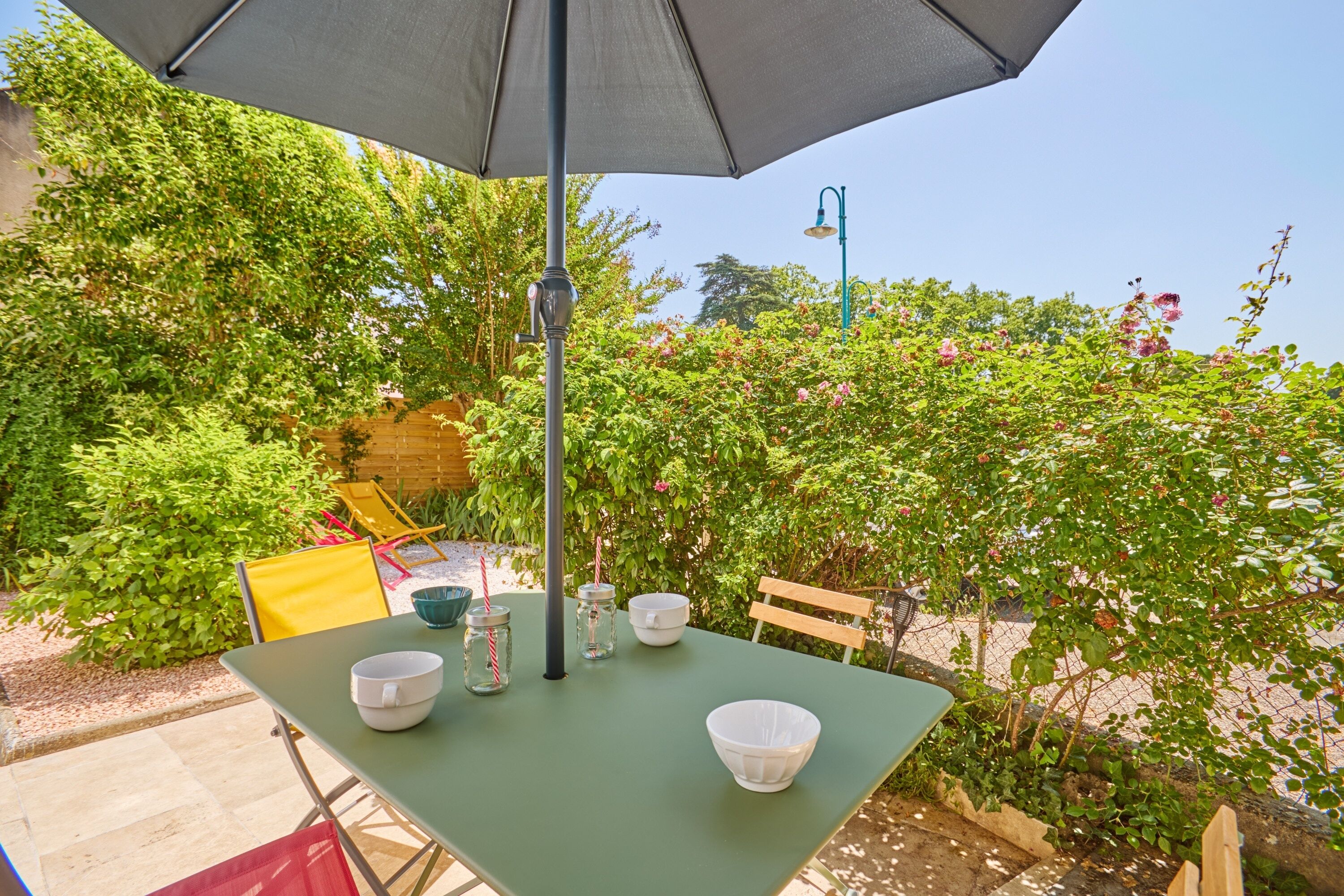 A patio table with a green tablecloth, a metal umbrella, and white bowls.