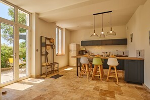 Een moderne keuken met een groot eiland, hangende lampen en een uitzicht door de glazen deur.