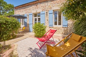 Een gebouw van steen met blauwe luiken, terrasmeubels en een patio met grind.