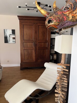 Une pièce comprenant une armoire en bois, un fauteuil blanc rembourré, une lampe et un élément décoratif au niveau de la tête de lit.