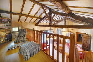 Ein Loft-Zimmer mit freiliegenden Holzbalken, einer Treppe, einem roten Sofa und einem gestreiften Ottoman.