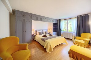 Ein Schlafzimmer mit einem Bett, zwei gelben Sesseln, einem grauen Kleiderschrank und einem Fenster mit Vorhängen.