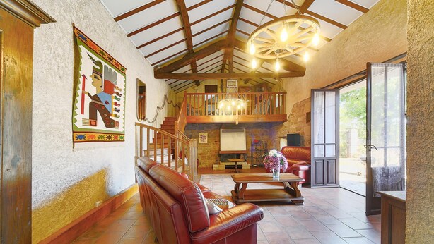 A spacious living area with a leather sofa, a wooden staircase, and a fireplace. - Le Frêne - Maison familiale au calme pour 10 (Vaour)