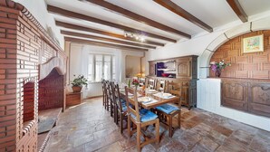 A dining area with a brick fireplace, wooden dining table, chairs, and a kitchen area with cabinets and a countertop. - Le Frêne - Maison familiale au calme pour 10 (Vaour)