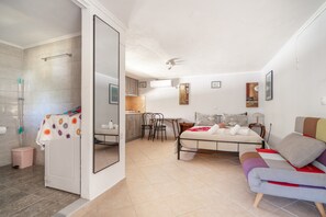 A bedroom with a bed, a chair, a small table, and a bathroom with a shower. - Mati Studio with Mountain View, Wi-Fi and Air Conditioning (Nydri)