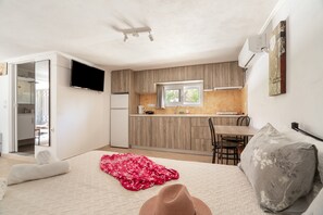 A compact room with a bed, a small desk, a chair, a window, and a kitchenette. - Mati Studio with Mountain View, Wi-Fi and Air Conditioning (Nydri)