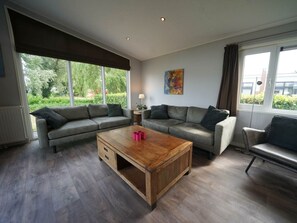 A modern living room with a sectional sofa, a wooden coffee table, and large windows with a view of greenery. - Holiday Home in Dordrecht With Terrace (Dordrecht)