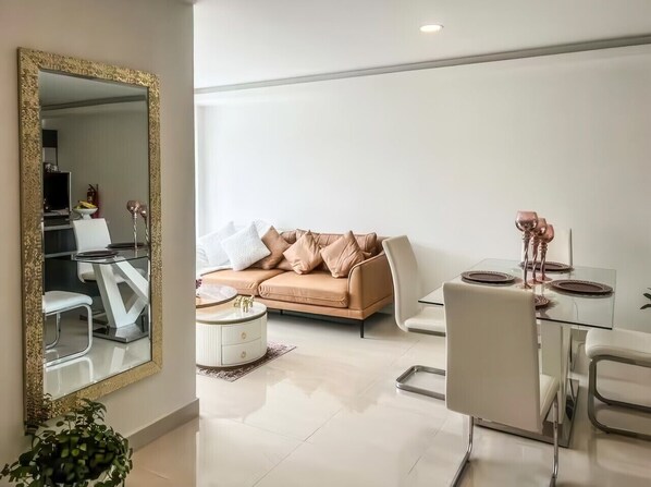 Een moderne woonkamer met een beige bank, een glazen eettafel en een grote spiegel.