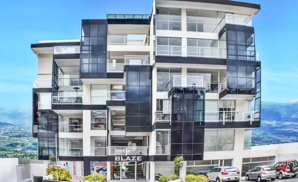 A multi-story building with balconies, a storefront labeled 'BLAZE,' and parked cars.