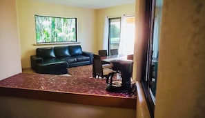 Una sala de estar con un sofá de cuero negro, un tapiz estampado, una mesa de centro y un ventanal con vistas a zonas verdes.