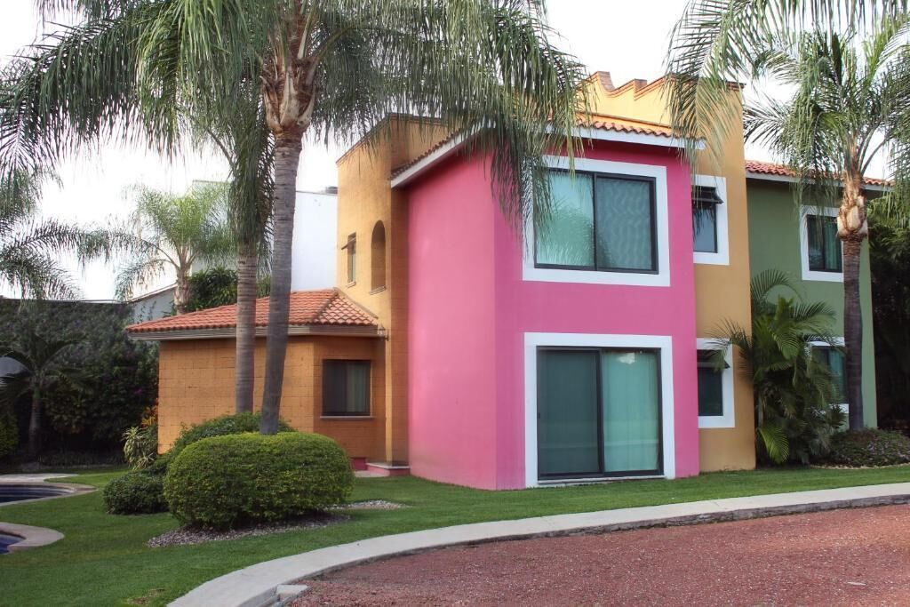 A multi-story building with a pink and yellow facade, large windows, and a well-maintained lawn.