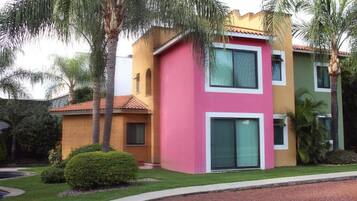 A multi-story building with a pink and yellow facade, large windows, and a well-maintained lawn.