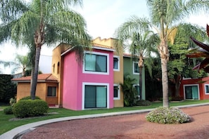 Un edificio de varios pisos con fachada rosa y beige, rodeado de palmeras y un césped bien cuidado.