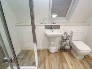 A bathroom with a glass shower door, a white sink, a toilet, and a small window above the sink. - Cwtch Treth (Newquay)