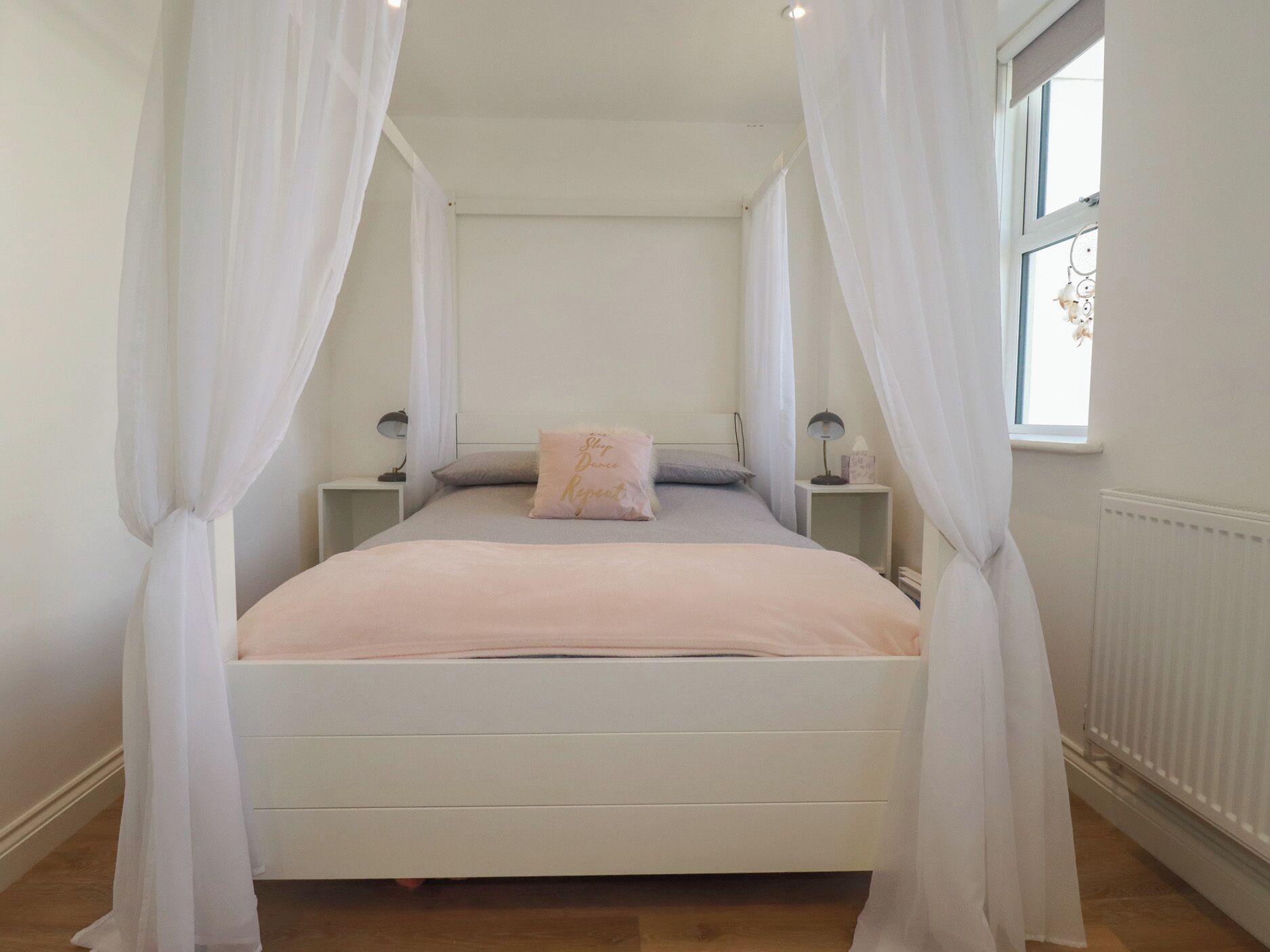 Un dormitorio con cama, cortinas blancas, lámparas de noche y ventana con vistas.