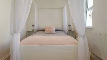 Un dormitorio con cama, cortinas blancas, lámparas de noche y ventana con vistas.