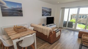 A modern living room with a dining area, a flat-screen TV, and large windows. - Cwtch Treth (Newquay)