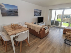 A modern living room with a dining area, a flat-screen TV, and large windows. - Cwtch Treth (Newquay)