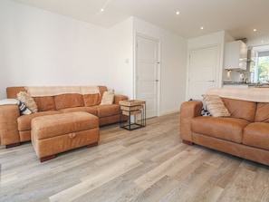 A modern living room with two sofas, a small side table, and a kitchen in the background. - Cwtch Treth (Newquay)