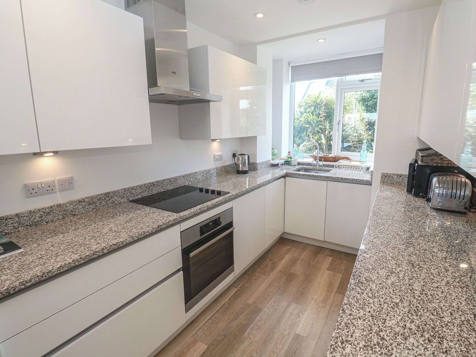 Una cocina moderna con muebles blancos, horno empotrado, estufa y ventana con vista a follaje.