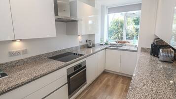 Una cocina moderna con muebles blancos, horno empotrado, estufa y ventana con vista a follaje.