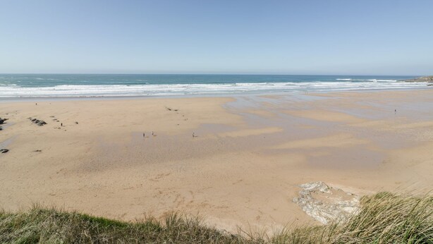 A beach with wet sand and waves, grassy dunes, and a clear sky. - Cwtch Treth (Newquay)