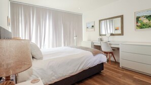 A hotel room with a bed, a desk, a chair, a lamp, and a dresser. - Cwtch Treth (Newquay)