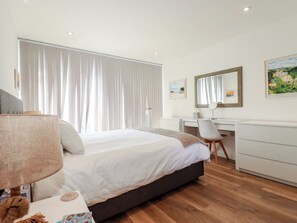 A hotel room with a bed, a desk, a chair, a lamp, and a dresser. - Cwtch Treth (Newquay)