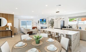 Une cuisine moderne dotée d’un îlot en marbre, un coin repas avec une table ronde et un espace de vie comprenant un canapé et un téléviseur.