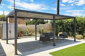 Ein überdachter Patio-Bereich mit Gartenmöbeln, einer Backsteinmauer und einem Rasen.