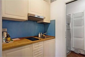 A kitchen with white cabinets, a blue backsplash, a stainless steel range hood, and a white door with a radiator. - Casestatedotnet - Seashell (Manarola)