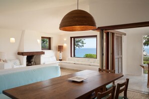 Ein modernes Wohnzimmer mit einem Holzesstisch, einer Couch, einem Kamin und einem großen Fenster mit Meerblick.