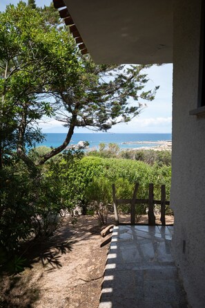 Ein steinbelagter Weg führt zu einer überdachten Fläche mit Blick auf das Meer und Grünflächen.