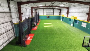 Un complexe sportif intérieur doté d’un terrain synthétique, de zones délimitées par des filets et d’un panier de basket.